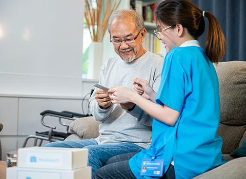 smiling senior man receiving assistance from caregiver while handling medication in a comfortable living room setting focusing on health care and support for the elderly