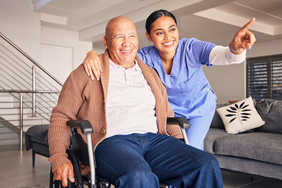 smiling elderly man in wheelchair receiving care from female nurse pointing at something in modern living room promoting health and wellness seven days a week