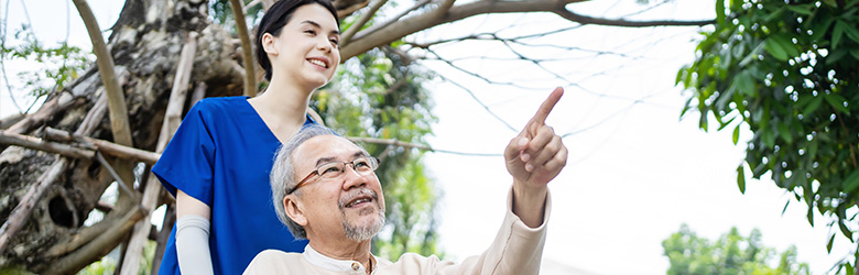 a caregiver assisting an elderly man outdoors both smiling and enjoying nature while the man points at something in the distance caregiver support for elderly