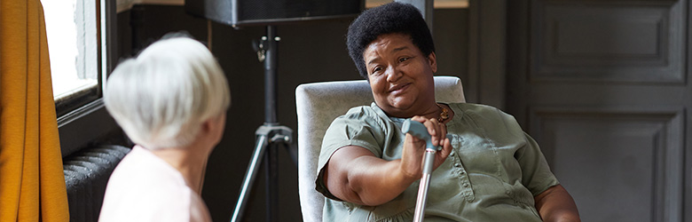 two women interacting in a room smiling and sharing conversation with a cane present