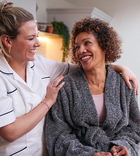 two women sharing a joyful moment one woman in a bathrobe smiling and laughing with a caregiver showing warmth and connection in a comfortable setting perfect for 4 care needs