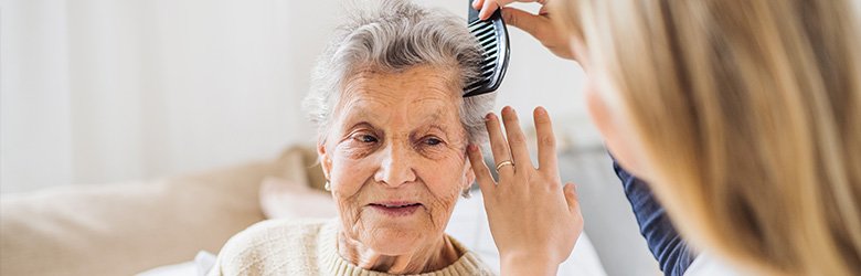 elderly woman smiling while having her hair combed in a bright room care for two elders