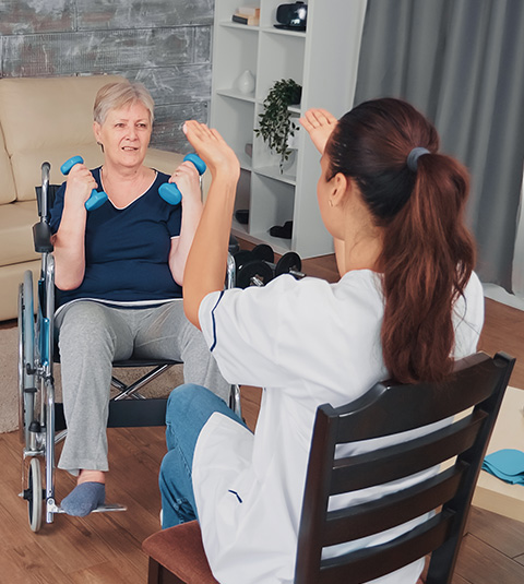 woman in wheelchair exercising with weights while caregiver demonstrates physical therapy techniques for improving strength and mobility through five key movements
